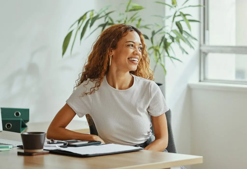 Black woman, modern finance office and smile by desk with corporate business financial document or accounting report. An African girl accountant, happy investment employee and international workplace